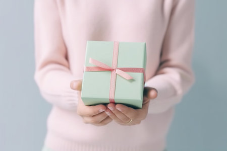 Woman holding a gift box with a pink ribbon on the grey backgroundの素材