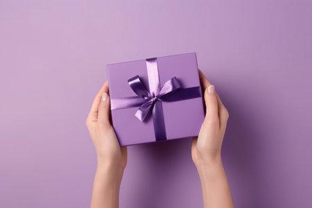 Female hands holding a gift box on a purple background, top viewの素材