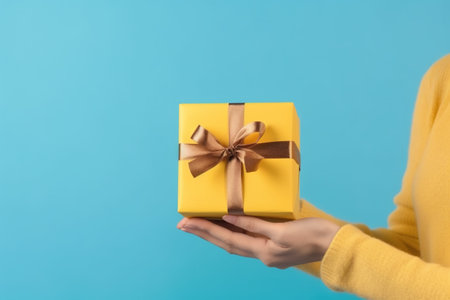 Woman holding yellow gift box on blue background, closeup. Holiday presentの素材