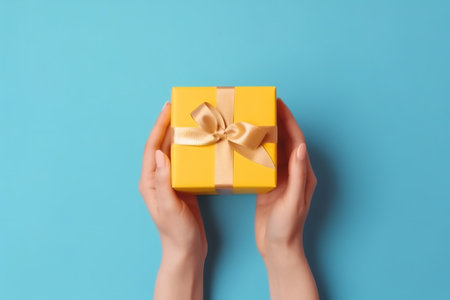 Female hands holding a yellow gift box on blue background. Top view.の素材
