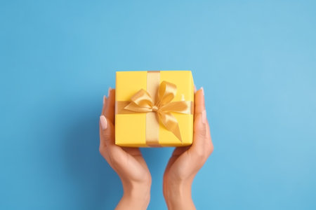 Female hands holding a yellow gift box on blue background. Top view.の素材