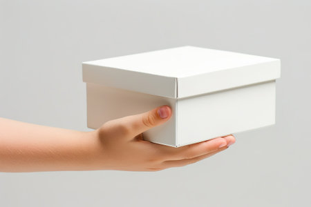 Female hand holding a white box isolated on gray background. Close up.の素材