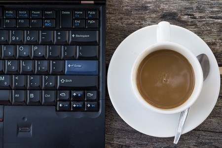 laptop with coffee is placed on a wooden table.の写真素材