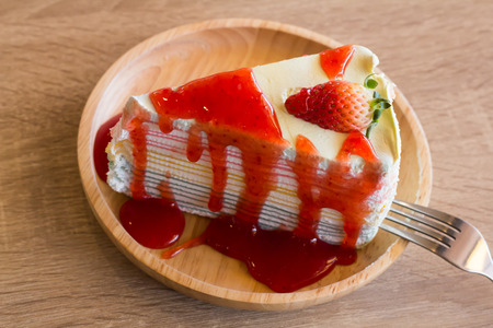 Crape cake dessert topped with sauce strawberry on wooden plate.の写真素材