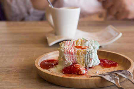 Crape cake dessert topped with sauce strawberry on wooden plate and blur white Coffee Cup.の写真素材