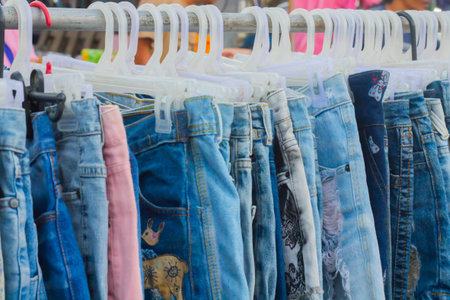 Row of hanged blue jeans fashionable clothes in the market. Jeans in plastic hanger. Showcase, sale,...
