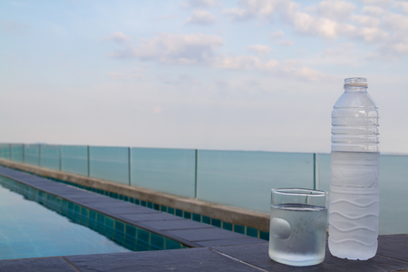 Glass of water and plastic water bottle by the pool.の写真素材