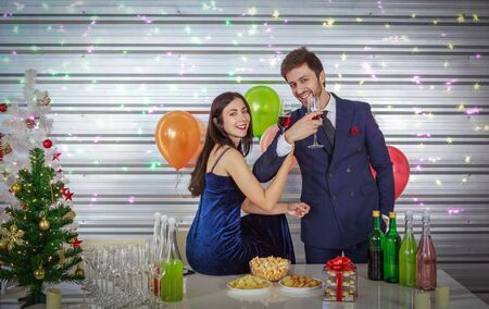 Smart man and beautiful woman holding glass of red wine on colorful light background - Christmas and Happy New Year party conceptの写真素材