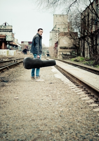 Young musician with guitar case in hand is looking away  Rear viewの写真素材