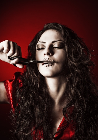 Horror shot  the strange girl with mouth sewn shut cutting the threadの写真素材