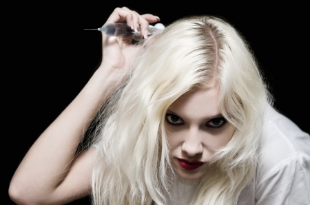 Beautiful young girl in the image of evil nurse with syringe in hand making a blowの写真素材