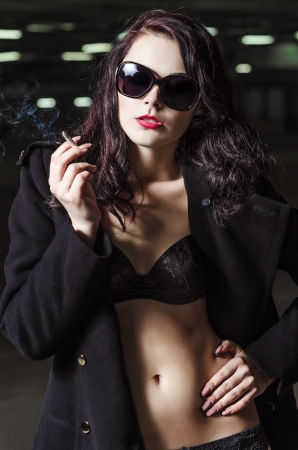 Closeup portrait of beautiful smoking young girl in black underwear and coatの写真素材