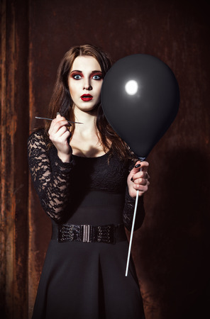 A strange scared girl is piercing a black balloon by needleの写真素材
