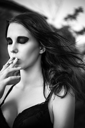 Dramatic portrait of a beautiful young girl smoking cigarette  Closeup の写真素材