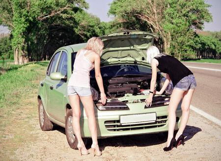 Two blonde girls stand by the broken car and donの写真素材