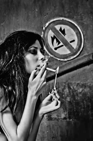 Beautiful young woman lights a cigarette near the  No fire and smoking  sign  Black and whiteの写真素材