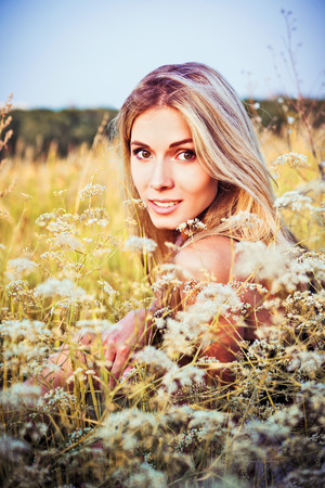  A beautiful smiling young girl sitting among the grass and flowersの写真素材