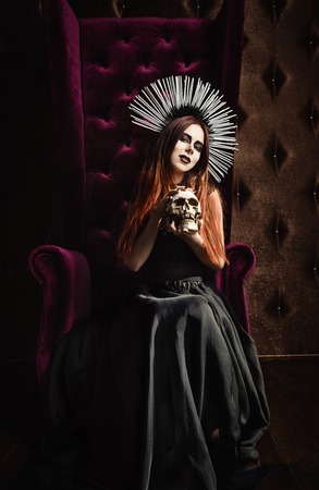 Horror photo: a beautiful gothic girl in black dress holds the skullの写真素材