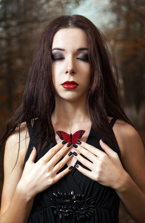 Lovely young girl with closed eyes holds a red butterfly in handsの写真素材