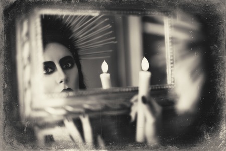 Beautiful goth girl holding candle in hand and looking into the mirror. Grunge texture effectの写真素材