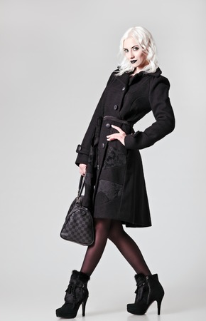 Studio fashion shot: beautiful girl in black coat and boots, with bag in handの写真素材