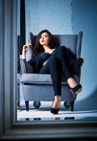 Portrait of a beautiful young woman sitting on chair and looking into mirrorの写真素材