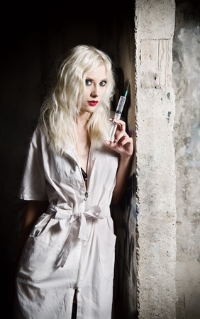 Beautiful young girl in the image of nurse with syringe in hand standing by the wallの写真素材