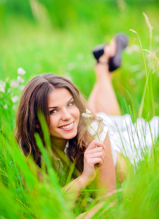 Happy smiling beautiful young girl lying among the grass and flowersの写真素材