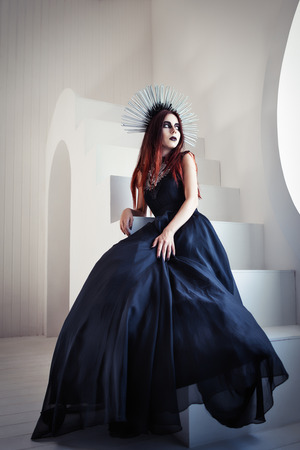 Gothic fashion: a beautiful young girl in black dress and headwear sitting on staircaseの写真素材