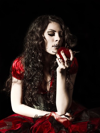 Horror shot: the strange scary girl with mouth sewn shut tries to eat an apple studded with nailsの写真素材