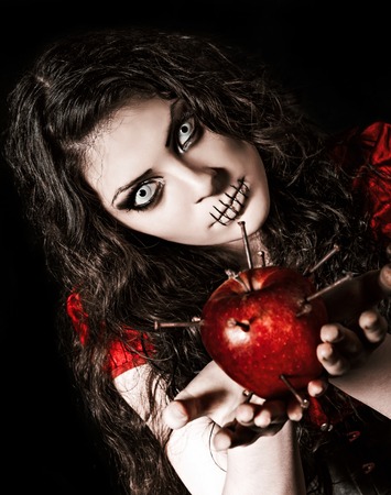 Horror shot: the strange scary girl with mouth sewn shut holds apple studded with nailsの写真素材