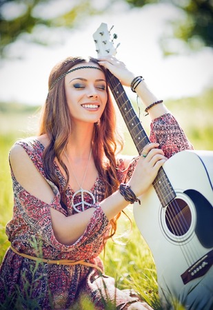 Portrait of a beautiful smiling hippie woman with guitar. Outdoor shotの写真素材