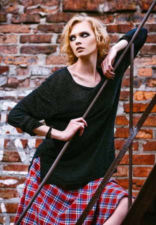 Grunge fashion: cute young woman in checkered skirt and jacket standing on the ladderの写真素材