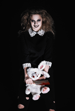 Horror shot: a scary wicked girl with rabbit toy and bloody cleaver in handsの写真素材