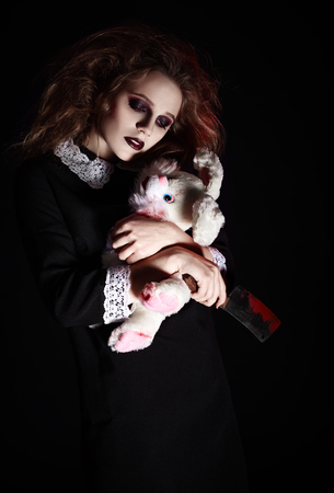 Horror shot: a sad gothic girl with rabbit toy and bloody knife in handsの写真素材