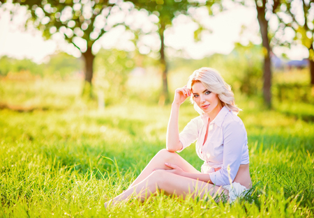 Smiling beautiful young girl sitting on grass in the gardenの写真素材