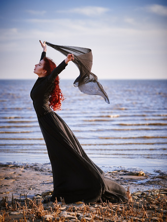 Beautiful sad goth girl with cloth in hands standing on the sea shoreの写真素材
