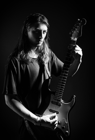 Dramatic studio portrait: a handsome long-haired young man (rock musician) playing the electric guitar. Black and whiteの写真素材