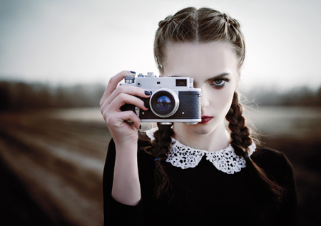 Lovely sad young girl photographing on the vintage film camera. Closeup outdoor portraitの写真素材