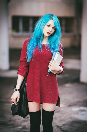 Portrait of cute smiling blue-haired grunge (rock) girl with books and cigarette in handsの写真素材