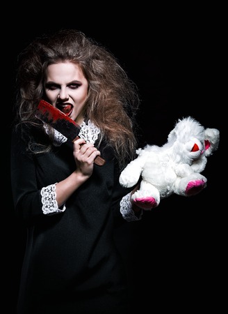 Horror shot: a scary demonic girl with torn rabbit toy and bloody knife in handsの写真素材
