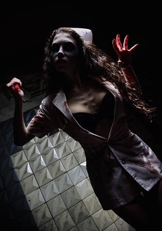 Horror shot: the grim wicked mad nurse (doctor) killing by bloody syringe. Zombie woman (living dead). Monster from nightmareの写真素材