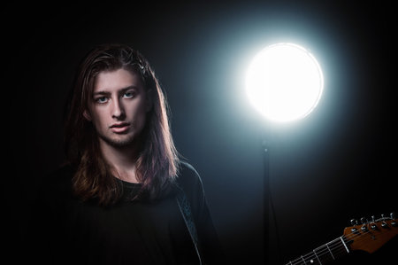 Studio portrait: a handsome long-haired young man (rock musician) with electric guitar