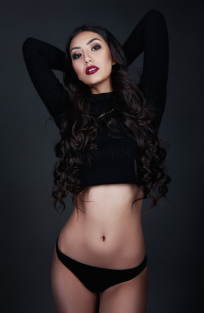 Studio fashion shot of the sexy young woman. Portrait of beautiful girl dressed in black panties and sweater. Seductive lady against gray backgroundの写真素材