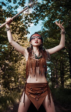 Outdoor portrait of the lovely young shamaness (witch doctor) with stick. Beautiful shaman (enchantress) making ritual. Sorceress praying in forestの写真素材