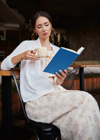 Beautiful girl sitting in restaurant and reading a book. Attractive young woman in cafe. Indoor portrait of cute ladyの写真素材