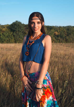 Outdoor portrait of the smiling cute young boho (hippie) girl in meadow at sunset time. Film grain addedの写真素材