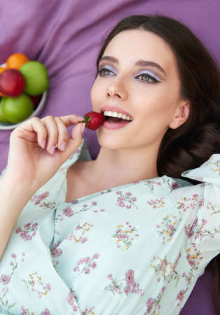 Pretty smiling girl eats strawberry. Close-up portrait of the beautiful young woman in dressの写真素材