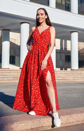 Street fashion: beautiful sweet girl in red dress and sneakers. Portrait of alluring smiling young womanの写真素材