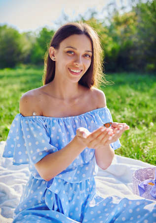 Picnic scene: happy smiling girl holds butterfly in hands. Portrait of joyful young woman in the gardenの写真素材